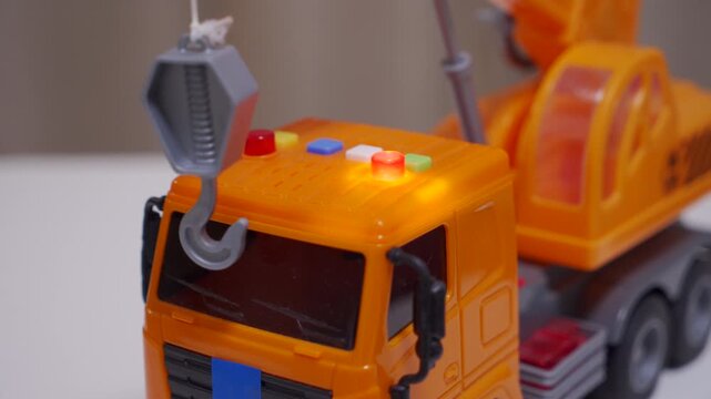 A plastic toy truck crane is shown from the front. The orange vehicle beeps in reverse as its red lights flash.