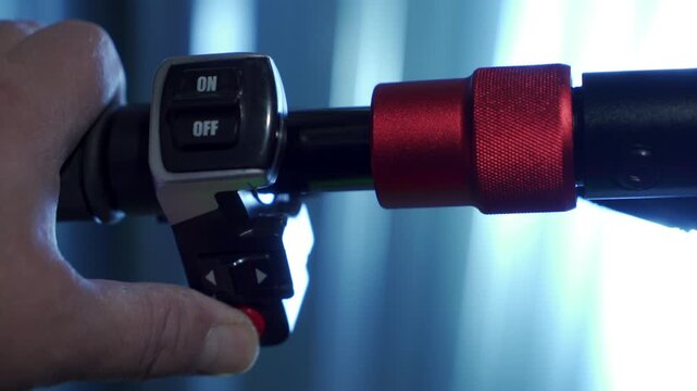 A person's thumb presses the red horn button on an electric scooter's handlebar controls. The scooter's signal lets out a loud, insistent beeping sound.