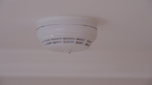 A plastic, ceiling-mounted smoke detector activates. The fire alarm emits a loud, piercing beeping sound to alert everyone of a potential fire.