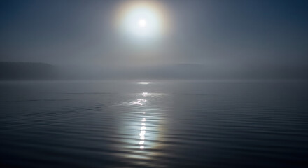 Sun halo over tranquil misty lake at dawn, reflecting light on the water