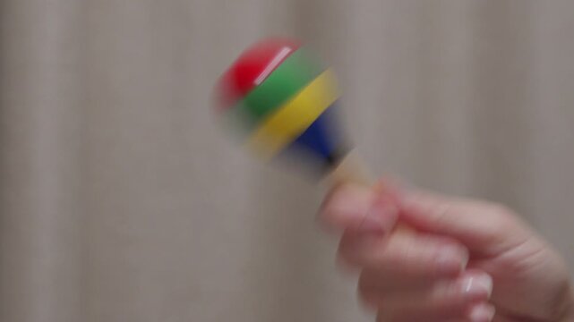 A hand shakes a colorful, wooden maraca. The instrument makes a soft, rhythmic rattling sound.