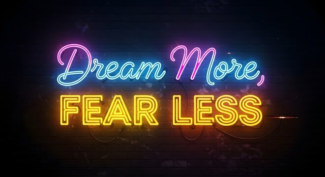 A vibrant neon sign displays the motivational message 'Dream More, Fear Less' in bright colors against a dark background, inspiring positivity and confidence