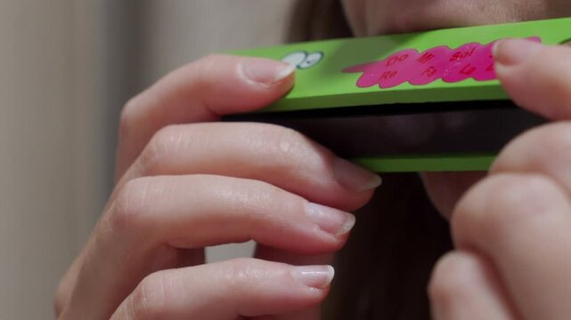 A person plays a green, wooden children's harmonica. The instrument produces a long, single, sustained note.