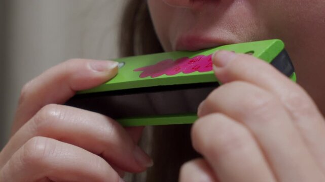 A person holds a wooden harmonica to their mouth. The person blows into the harmonica. A single, distinct musical note is produced.
