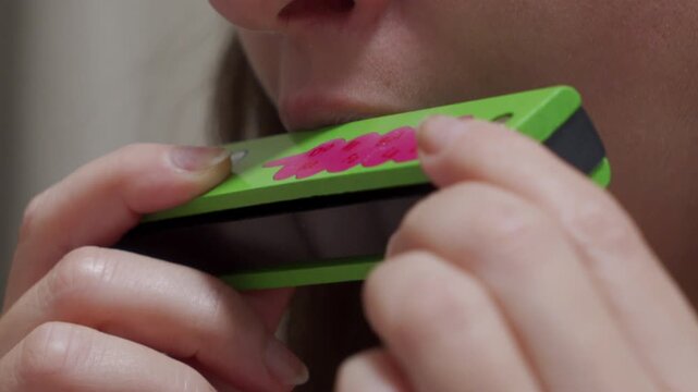 A person holds a wooden harmonica to their mouth. The person blows into the harmonica. A single, distinct musical note is produced.