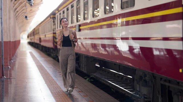 Asian young adult woman traveler carrying backpack waiting train station platform enjoys peaceful journey planning trip