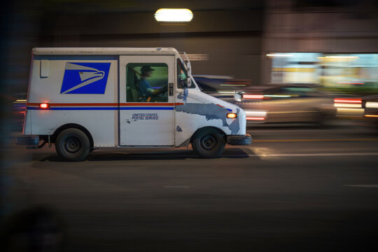 LOS ANGELES, CA - March 3 2025: USPS delivery truck driving in city traffic at night. Blurred motion.