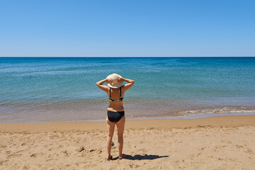 Rear view of a retired woman wearing a hat standing on the seashore enjoying the beautiful view.