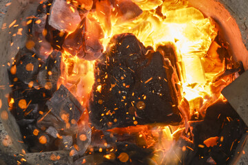 Close up view of burning coal in fire pit. intense fire produces hot flames, glowing embers, and flying sparks, creating powerful and energetic feeling
