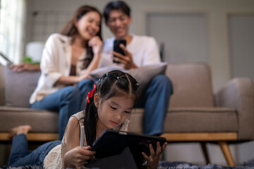 Asian child using tablet with parents relaxing in background