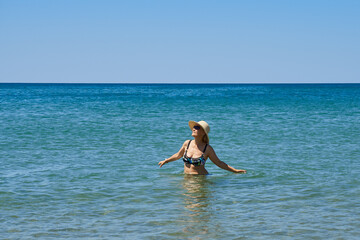 A retired woman in a swimsuit and hat enjoys the sea and sun.