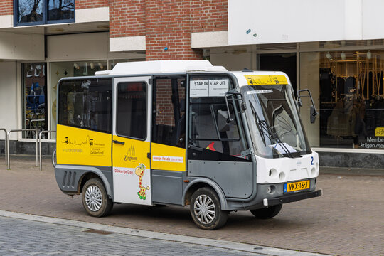 "Stap in Stap uit" electric city bus in Zutphen, a small, accessible public transport vehicle painted yellow and grey, with a giraffe decal. Zutphen Netherlands, 7 November 2025.
