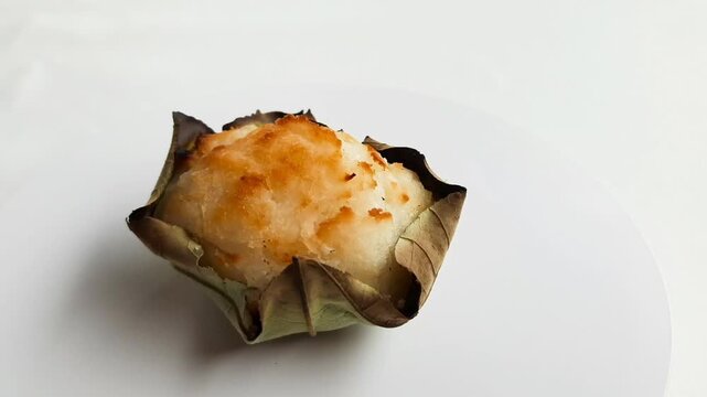 Traditional Minang baked bika cake served on a waru leaf, a sweet coconut snack from West Sumatra, Indonesia, isolated on white background. close up