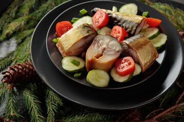 Smoked mackerel with fresh cucumbers, tomatoes and green onions on a black plate.