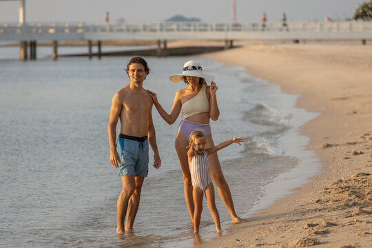 Happy family standing on beach during summer vacation, smiling and enjoying sunny seaside time together. Natural lifestyle moment of parents and child bonding near ocean waves.