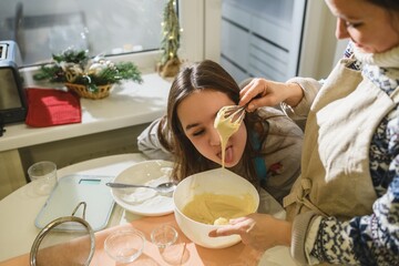 Girl tasting cake batter while baking with mother at Christmas.