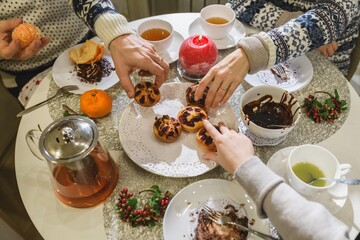 Family sharing homemade cupcakes and tea at festive Christmas table.