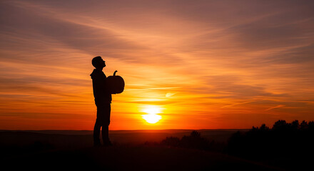 Fototapeta premium Silhouette Child Carrying Bag Standing in Sunset Landscape During Vibrant Orange Sky