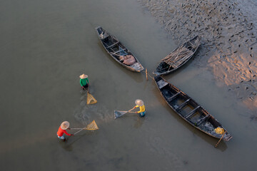 Top view of three unidentified men using fishing nets in shallow water