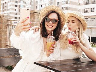 Two young beautiful smiling hipster female in trendy summer straw hats. Sexy carefree women holding...