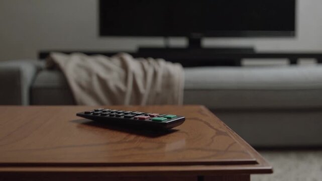 Cozy living room scene with remote on wooden table and soft blanket draped on sofa