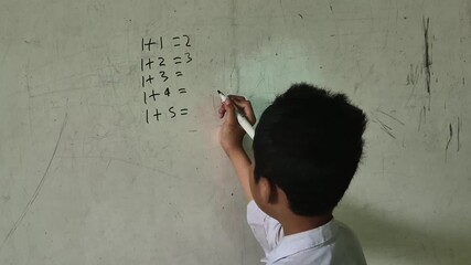 A boy student An elementary school is writing numbers to answer a math problem on the board using marker pen - Powered by Adobe