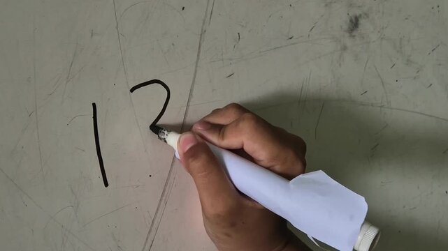 The hand of a boy elementary school student is writing numbers 123 on the classroom board using marker pen.