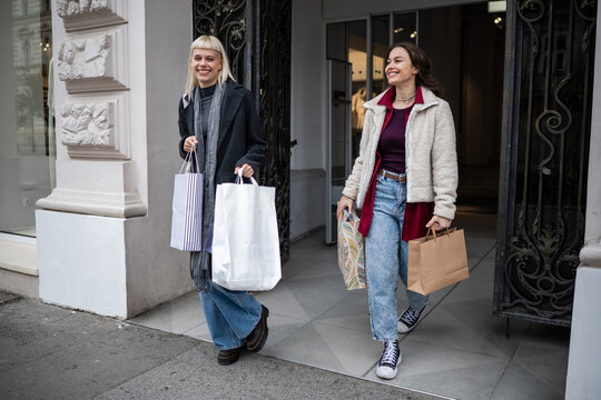 Two young women exiting a store carrying shopping bags