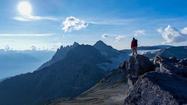 Hiker Standing On A Rocky Peak Over Looking Snowy Mountain Range At Dusk Adventure