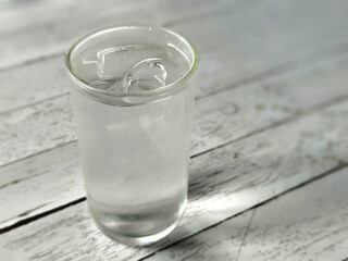 A clear glass of cold water with ice cubes, placed on a white wooden table.
