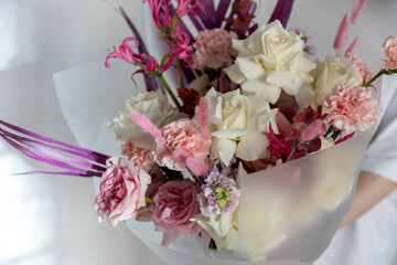 A luxurious bouquet close-up, showcasing a mix of soft pink and white roses, blush carnations, and dark magenta foliage textures
