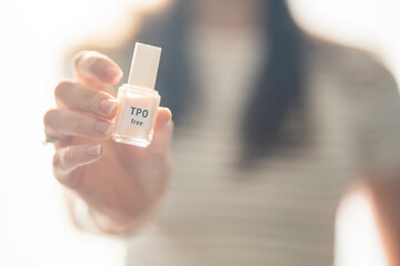 Woman holding a bottle of TPO free gel polish in bright natural light. Safe manicure product...