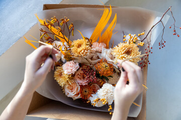 Top view of a florist's hands tying a rustic string around a rich orange and peach bouquet in a craft paper delivery box near a window