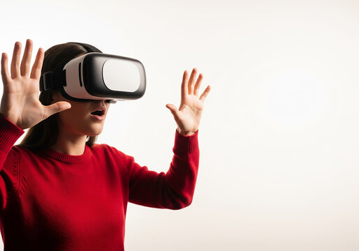 Young woman in a red sweater wearing a virtual reality headset with an amazed expression, raising her hands to interact with the simulated environment on a plain white background. - Powered by Adobe