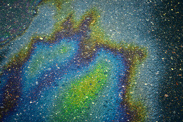 Iridescent oil slick spreading vibrant rainbow colors across wet asphalt pavement