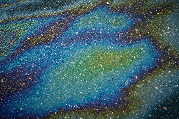 Fototapeta premium Oil slick on asphalt creating colorful iridescent patterns, symbolizing pollution and environmental impact.