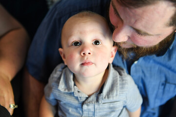Toddler looks up while sitting in father's lap indoors