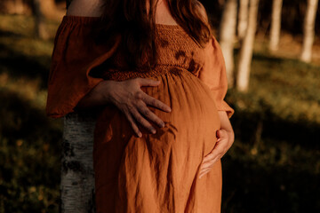 Pregnant woman in orange dress holding belly outdoors
