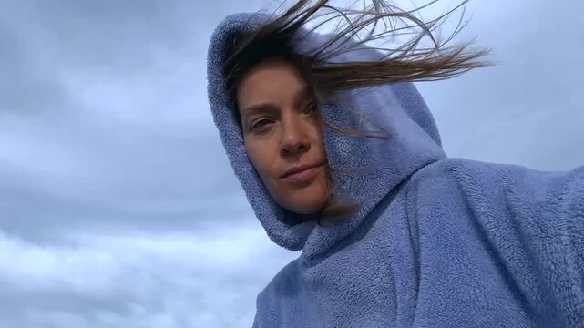 Woman with Hooded Poncho Standing Outdoors with Wind in Hair