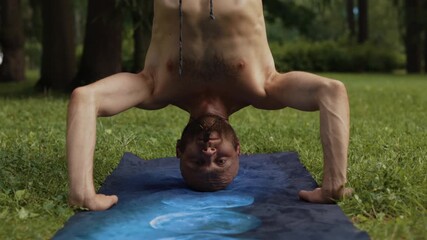 Man practices headstand yoga in a peaceful park setting