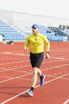 Runner in yellow sweatshirt and blue cap on stadium