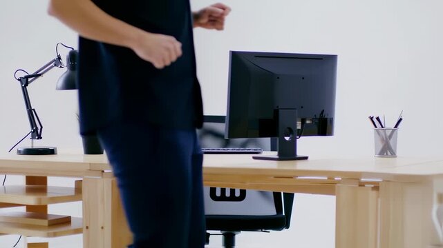 A minimalist office workspace with desk, monitor, lamp, potted plant, and a person