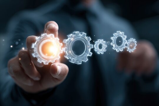 A human hand gently presses or interacts with a glowing, intricate digital gear icon against a dark, atmospheric background. This vibrant gear, illuminated with a warm orange light, stands out among a