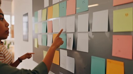 Two women collaborating and brainstorming ideas using colorful sticky notes on a glass wall in an office setting. - Powered by Adobe