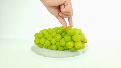 an asian woman's hand holding one sweet green shine muscat grape on a round white plate, isolated on a white background