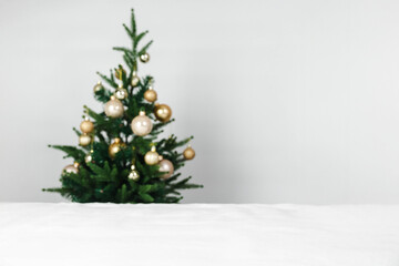 Christmas holiday background. White snow in the foreground with copy space and a blurred minimalist Christmas tree and golden ornaments.