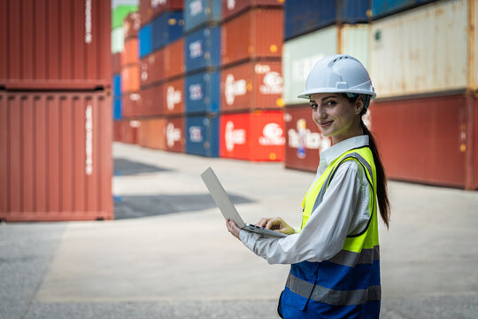 A woman wearing a hard hat and safety vest is using a laptop computer. She is smiling and she is enjoying her work
