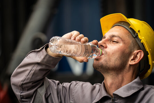 A man in a yellow hard hat drinks water from a bottle. Concept of hard work and the importance of staying hydrated while on the job