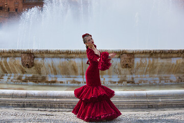 A beautiful woman dancing flamenco in a square in Seville, Spain. She is wearing a red dress with...