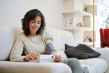 confident Senior woman monitoring blood pressure at home sitting on the couch